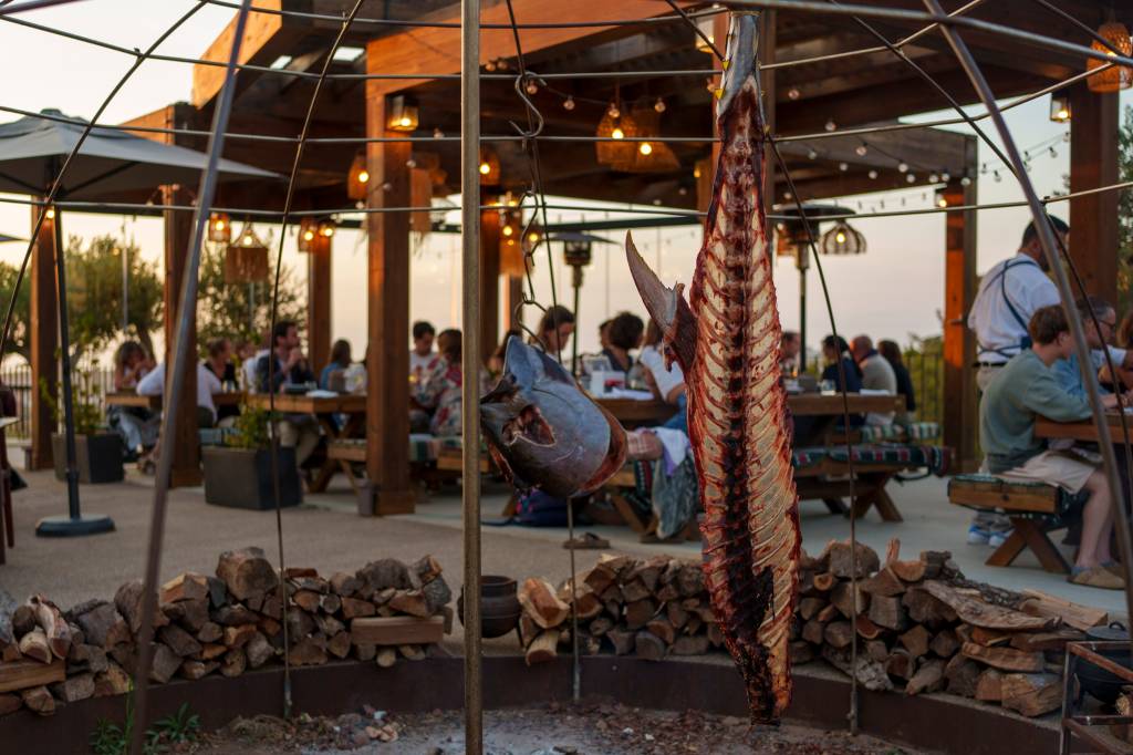 _1NC8819-1 Imagem do restaurante com mesas ao ar livre e pessoas a jantar, e o esqueleto de um enorme atum no fogo de chão